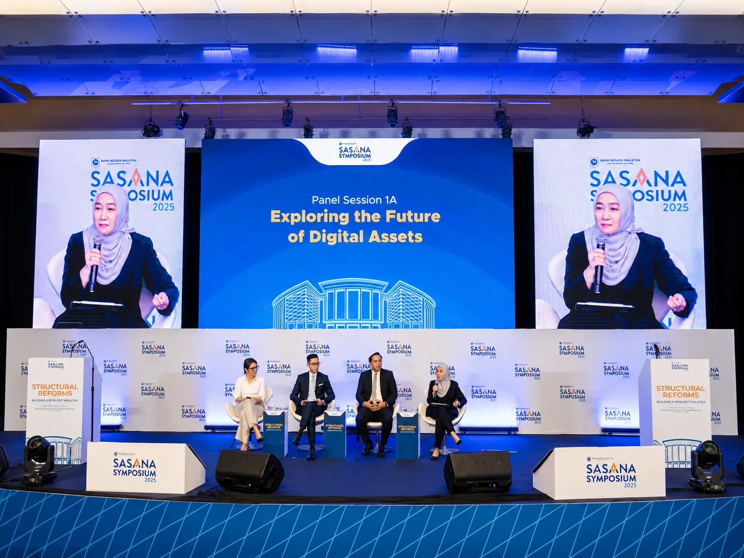 Sasana Symposium 2025 – panel session on Digital Assets with matching LED screens flanking the main stage